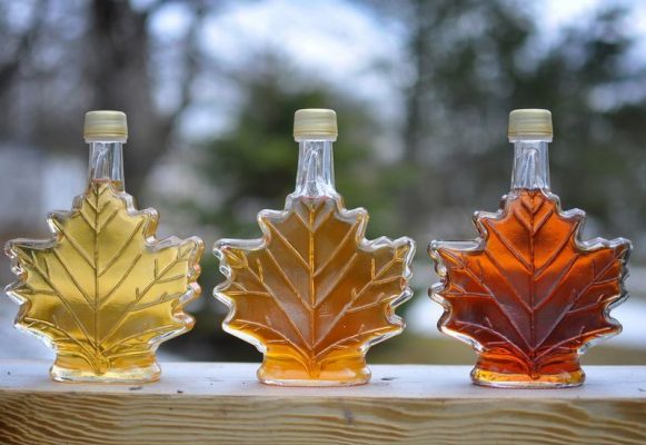 Three maple leaf-shaped bottles of maple syrup